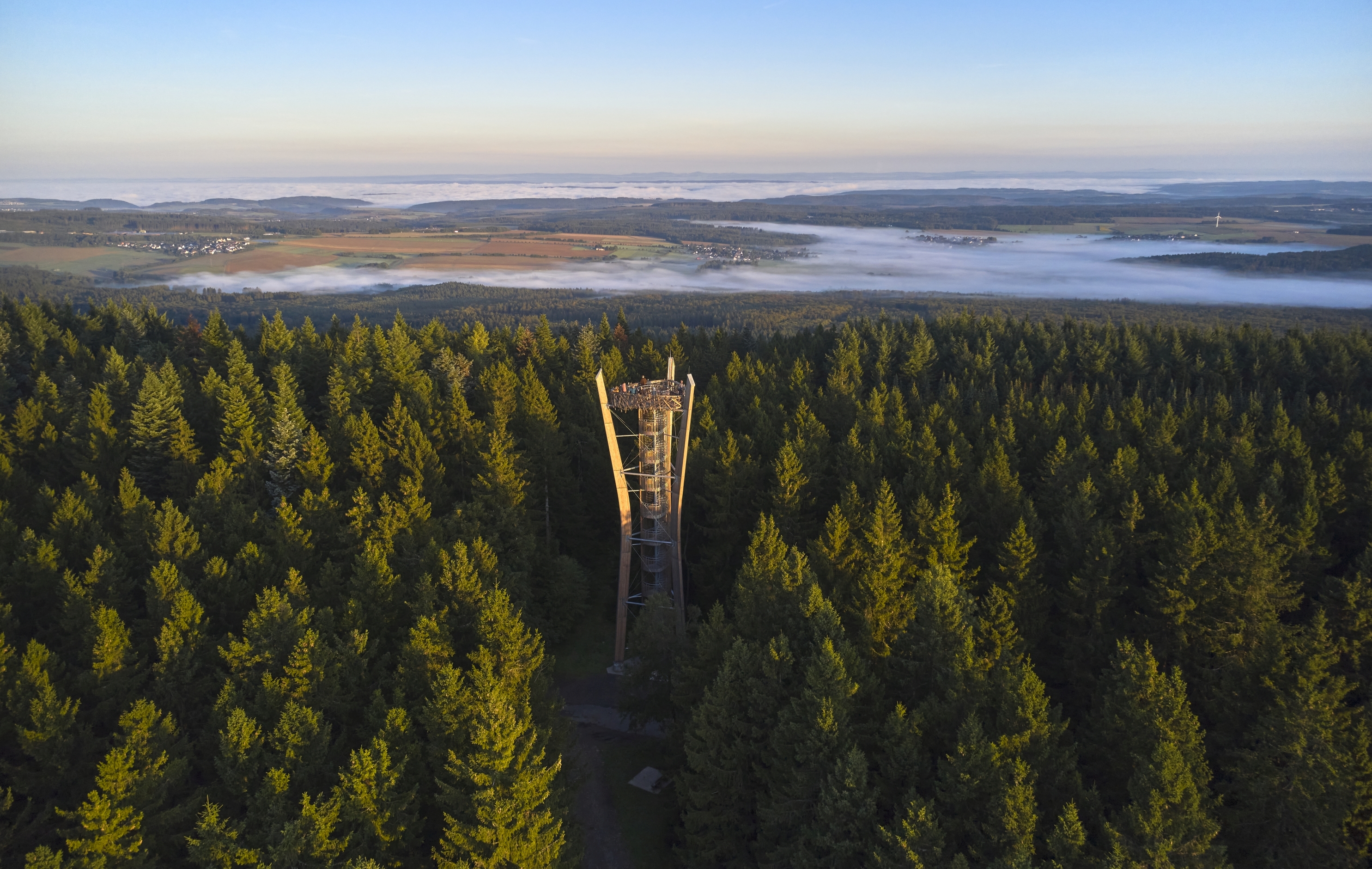 Idarkopfturm aus der Luft Luftbild des Idarkopfturmes inmitten von Wald. Auf dem Turm stehen ein paar Personen. In Hintergrund sind in Nebel ein paar Orte zu sehen.