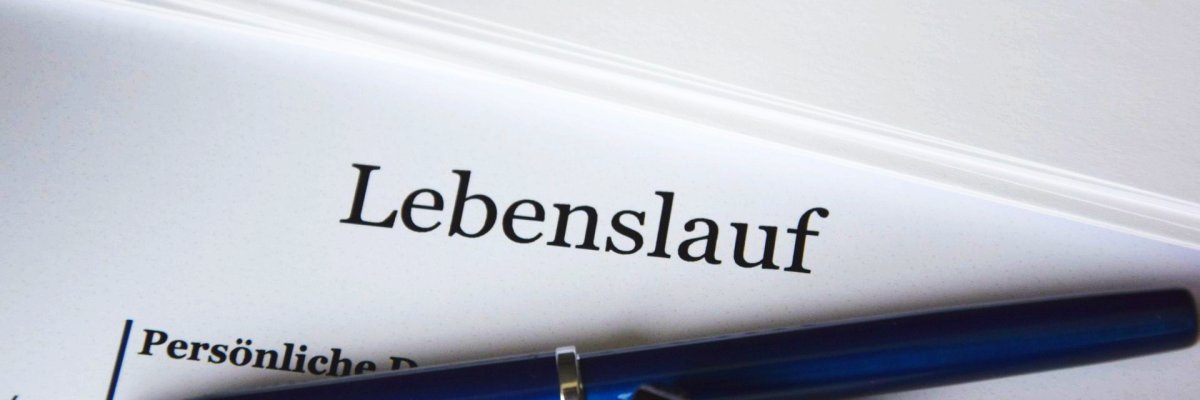 Ein Blatt Papier mit den Worten Lebenslauf, Persönliche Daten, Profil und darauf liegend ein blauer Kugelschreiber und ein schwarze Brille