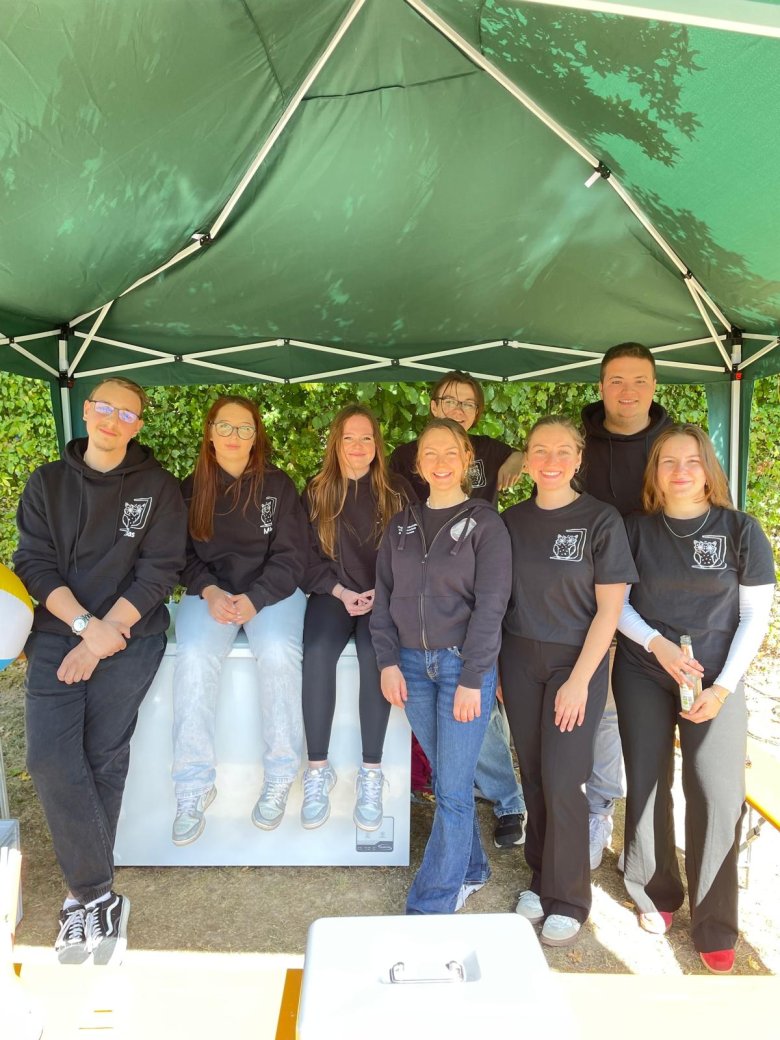 Gruppe von acht Personen in schwarzer Kleidung unter grünem Pavillon im Freien