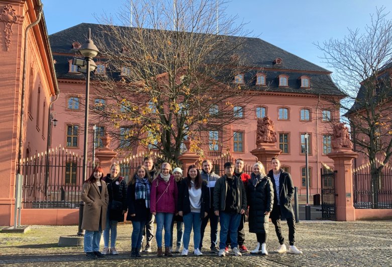 Jugendbeirat Tagungswochenende Mainz 2022 Gruppe von Menschen steht vor einem historischen Gebäude mit rotem Sandstein und einem kahlen Baum im Innenhof