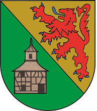 In schräggeteiltem Schild vorne in Grün ein silbernes Fachwerkhaus mit Glockenturm , schwarzen Fenstern und schwarzer Türe , hinten in Gold ein blaubewehrter und – gezungter roter Löwe.