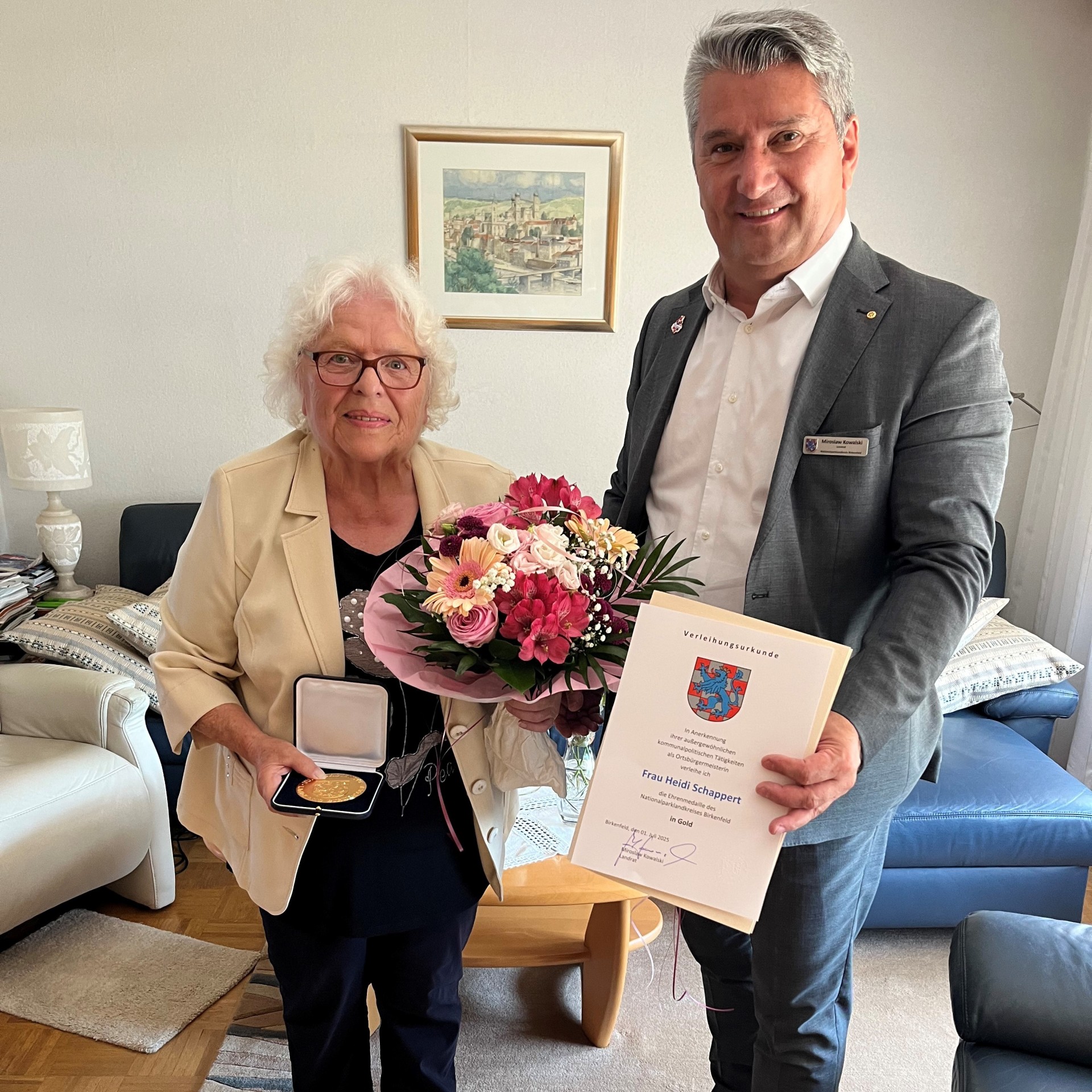 Auf dem Bild überreicht Landrat Kowalski die Ehrenmedaille in Gold an Frau Heidi Schappert zusammen mit einer Ernennungsurkunde und einem Blumenstrauß.