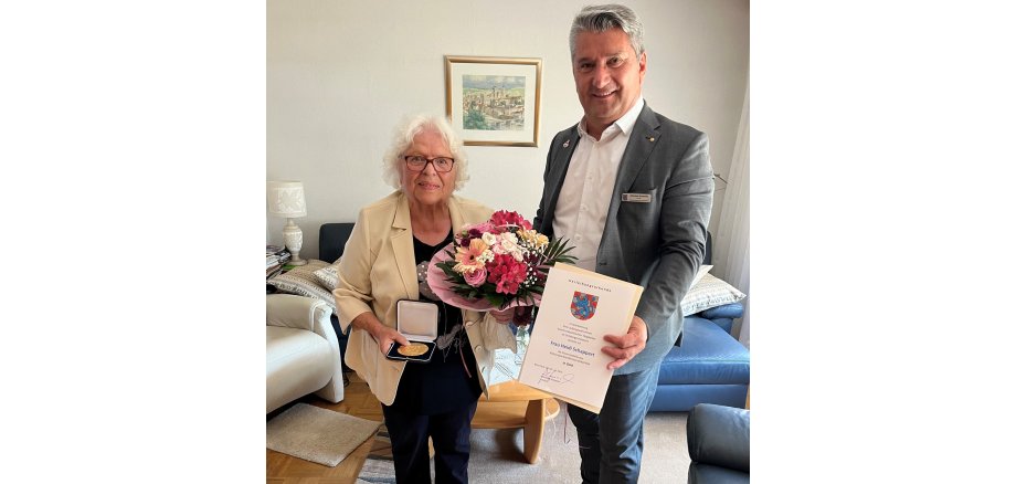 Auf dem Bild überreicht Landrat Kowalski die Ehrenmedaille in Gold an Frau Heidi Schappert zusammen mit einer Ernennungsurkunde und einem Blumenstrauß.