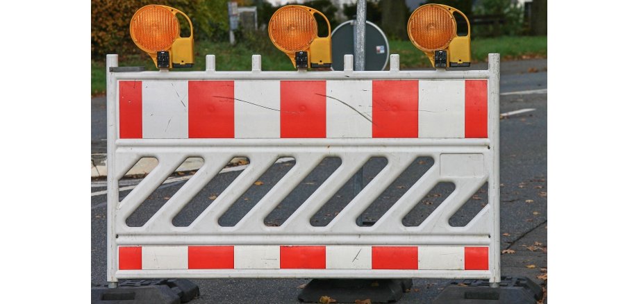 zu sehen hier ist eine Straßenabsperrung mit einem weißen gitter welches mit orangenen Streifen versehen ist und 3 orangefarbene Leuchten obendrauf hat
