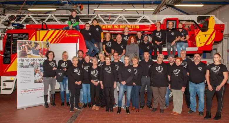 Gruppenfoto der Akteure vom Filmspot Heimatliebe (Landlebenrockt) vor dem Feuerwehrauto mit den neuen T-Shirts
