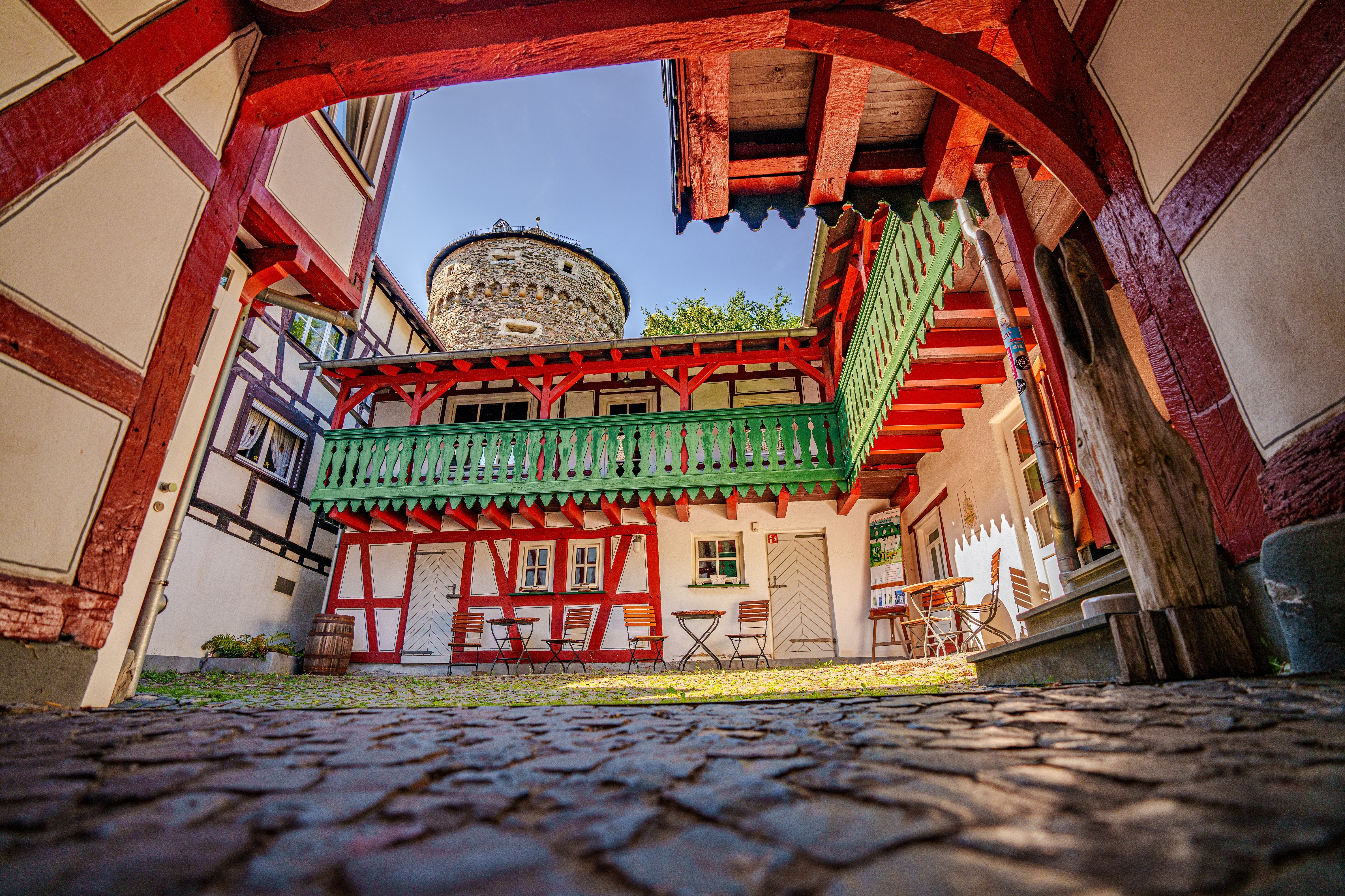 Innenhof eines Fachwerkhauses mit grünem Balkon und rundem Steinturm im Hintergrund