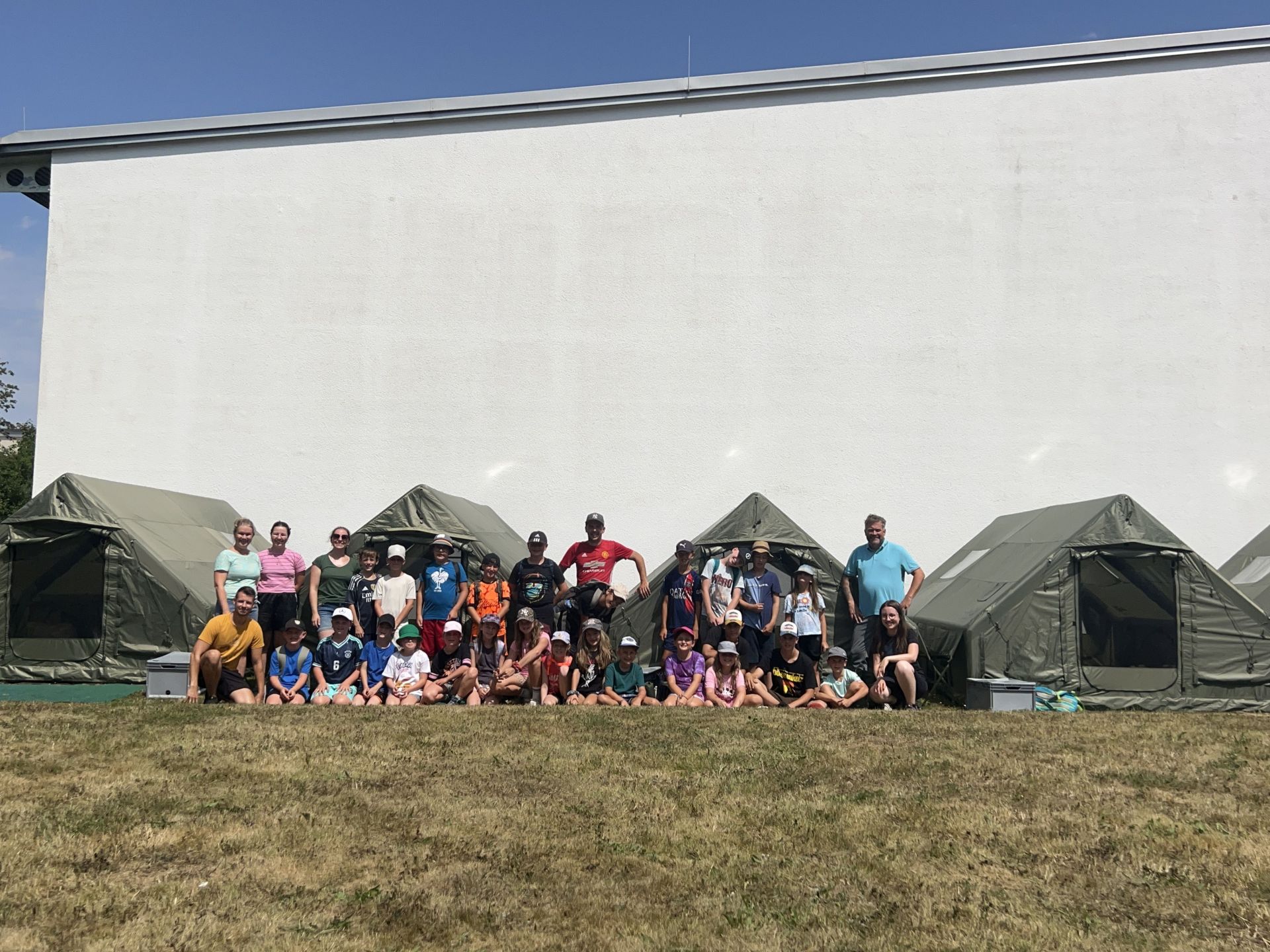Jugendpflege - Outdoorcamp - Kinder mit Betreuer*innen vor den Outdoorzelten 