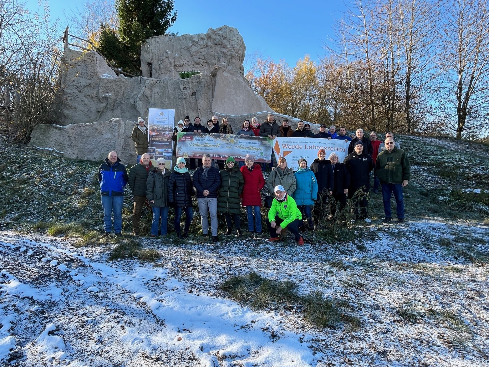 Gruppe von Personen mit Bannern vor einer Ruine inmitten von Wald, Wiesen bedeckt mit Schnee
