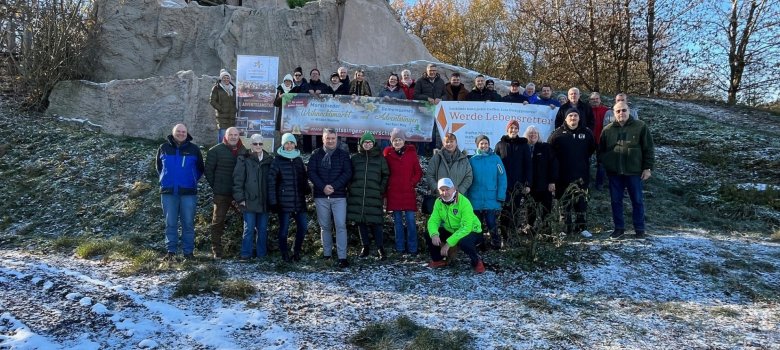 Gruppe von Personen mit Bannern vor einer Ruine inmitten von Wald, Wiesen bedeckt mit Schnee
