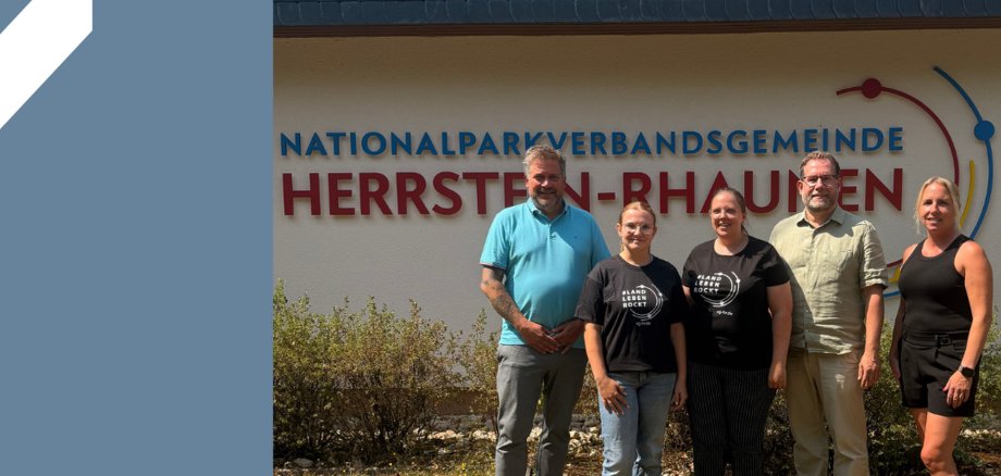 Fünf Personen stehen vor einem Gebäude mit der Aufschrift 'Nationalparkverbandsgemeinde Herrstein-Rhaunen' und lächeln in die Kamera Fünf Personen stehen vor einem Gebäude mit der Aufschrift 'Nationalparkverbandsgemeinde Herrstein-Rhaunen' und lächeln in die Kamera